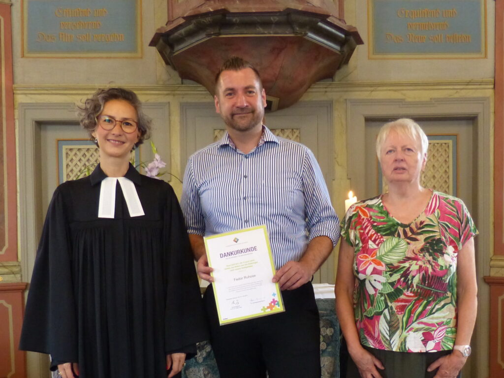 Das Foto zeigt Dekanin Arami Neumann, Fedor Ruhose und Kirchenvorstandsvorsitzende Ulrike Boppré. Sie stehen vor dem Altar. 